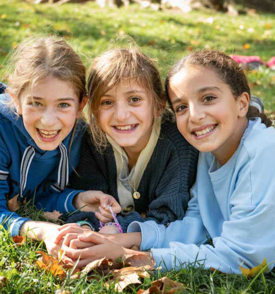 3 petites filles dans un parc souriantes face à l'objectif