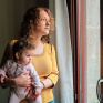 Une maman portant son bébé dans ses bras et regardant par la fenêtre de son appartement